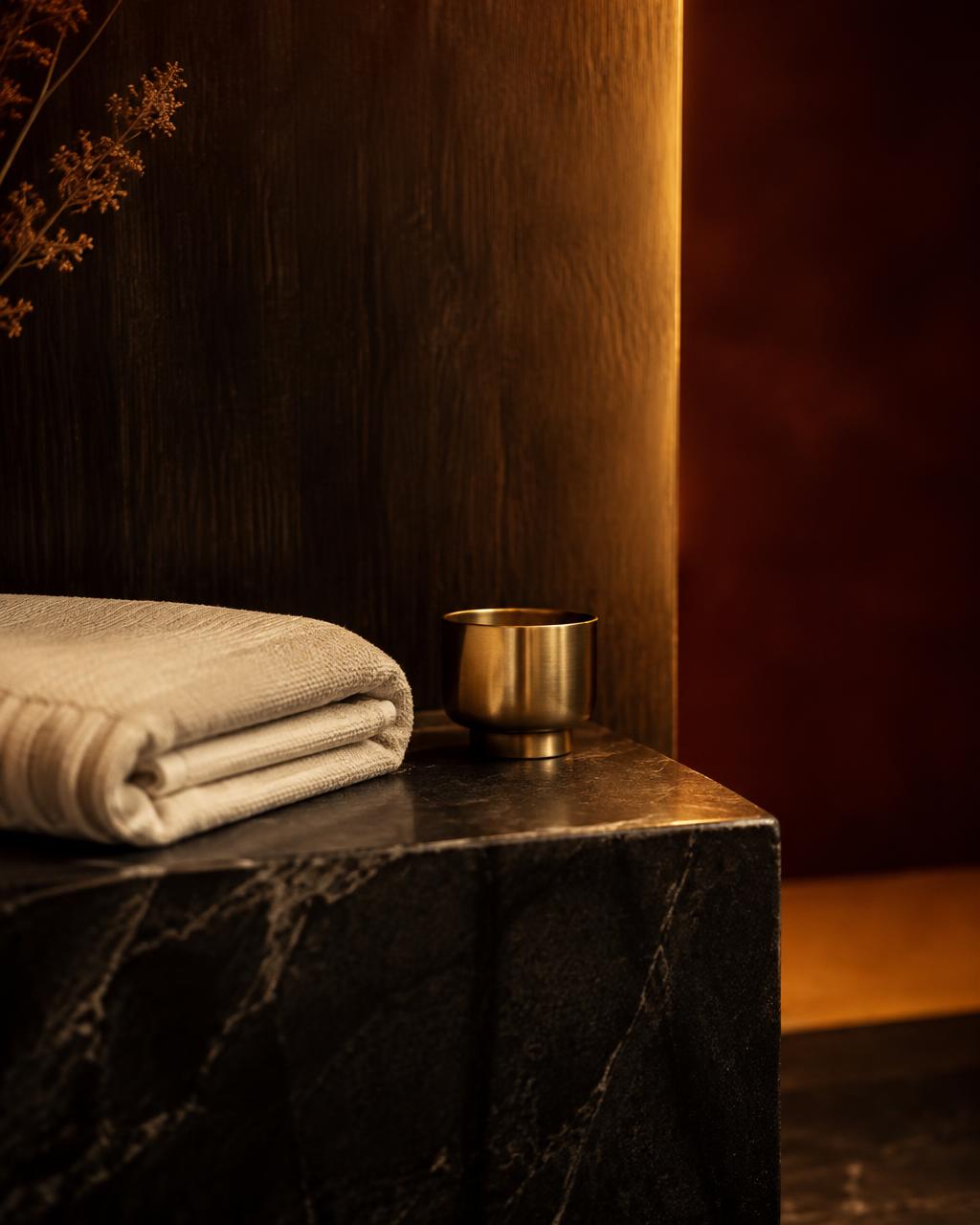 Folded linen and a brass vessel on dark stone in warm light
